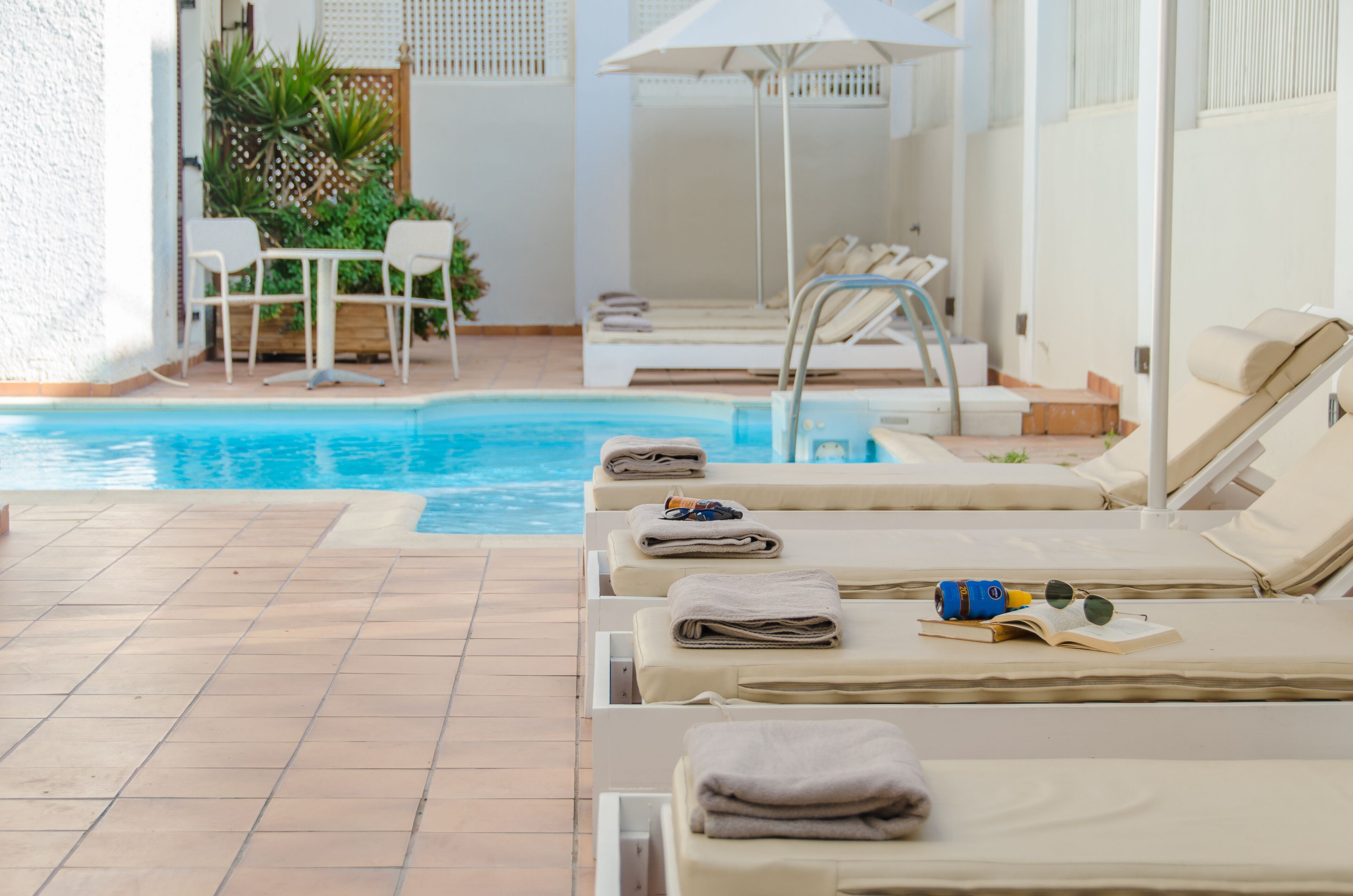 Uma área à beira da piscina com espreguiçadeiras, uma mesa pequena e uma piscina.