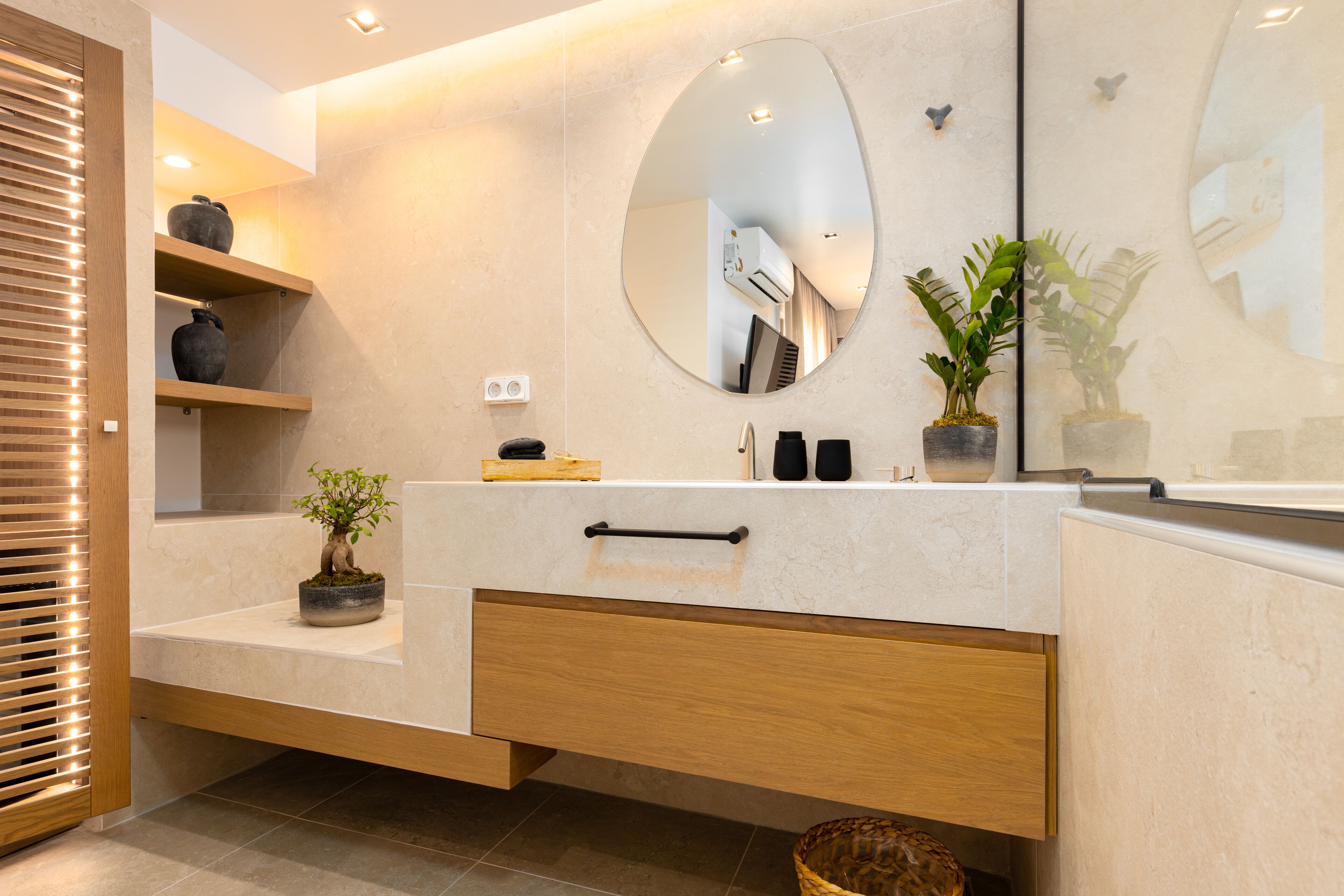 A modern bathroom with a wooden vanity, a large mirror, and a potted plant.