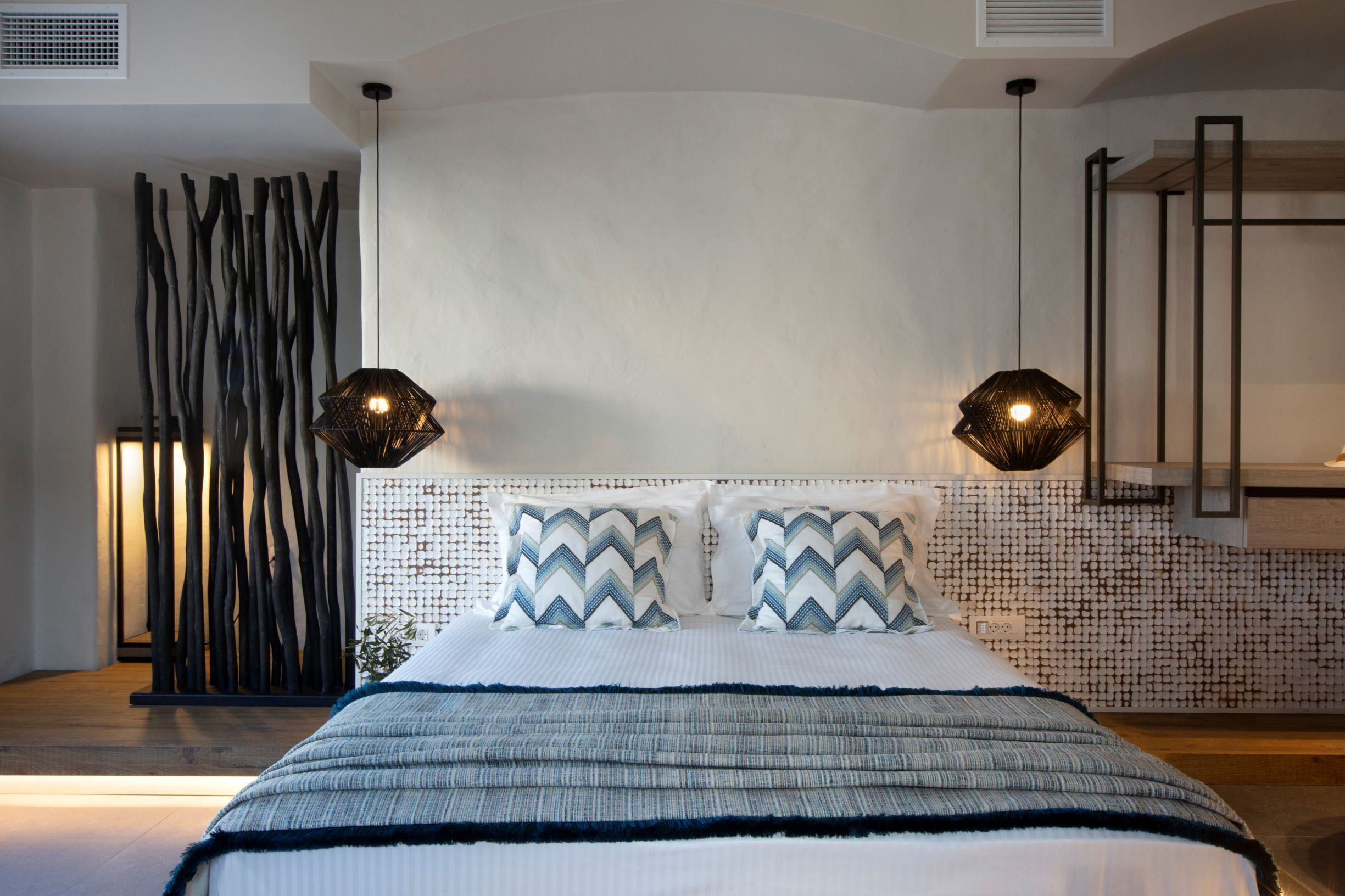 A bedroom with a bed, two wall-mounted lamps, a decorative wall, and a wooden floor.