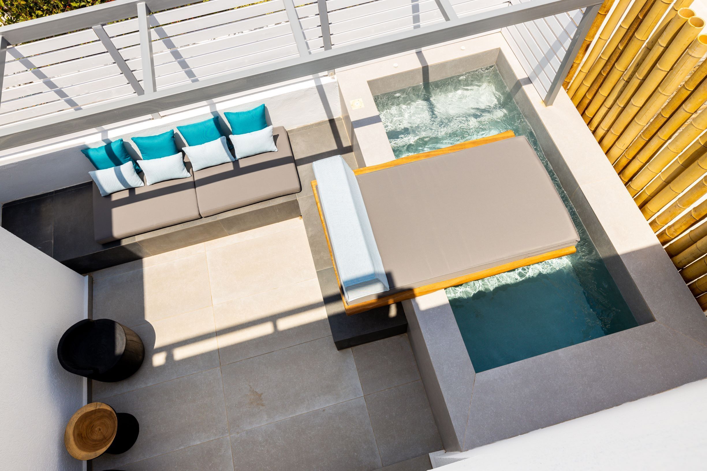 A rooftop pool area with a seating area, a small hot tub, and a bamboo fence.