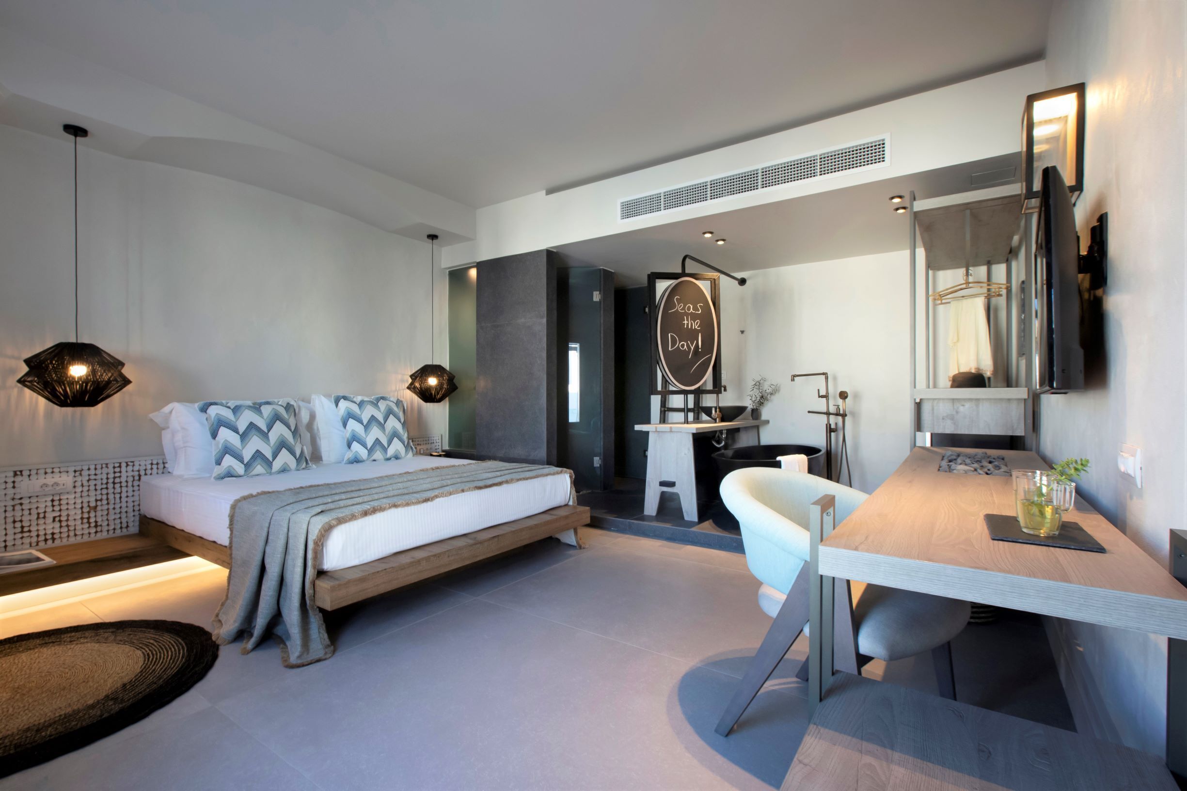 Une chambre d’hôtel moderne équipée d’un lit, d’une table de chevet, d’un bureau, d’une chaise et d’un miroir.