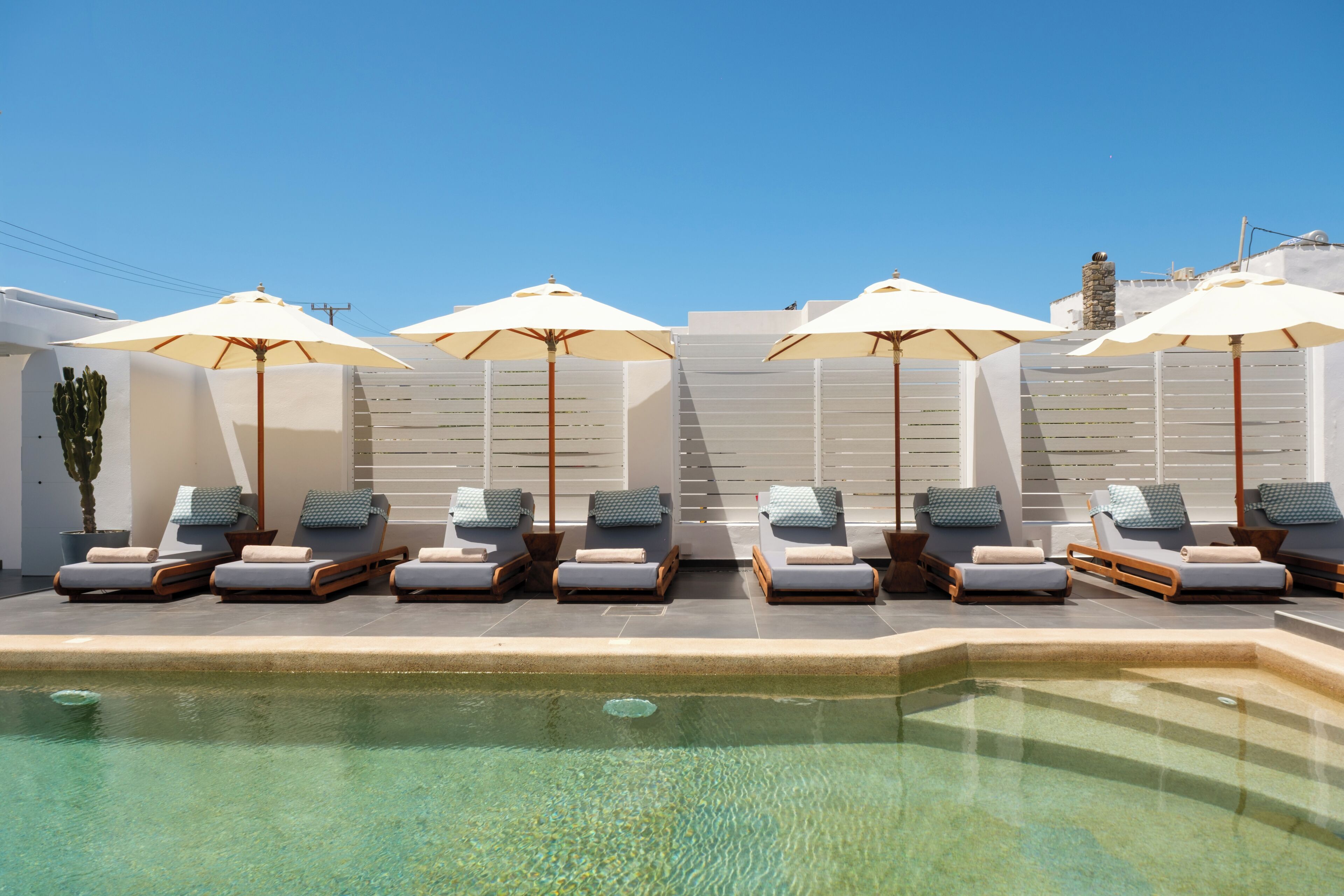 Un espace aménagé au bord de la piscine, avec des chaises longues et des parasols, un ciel bleu dégagé et un mur de pierre en arrière-plan.
