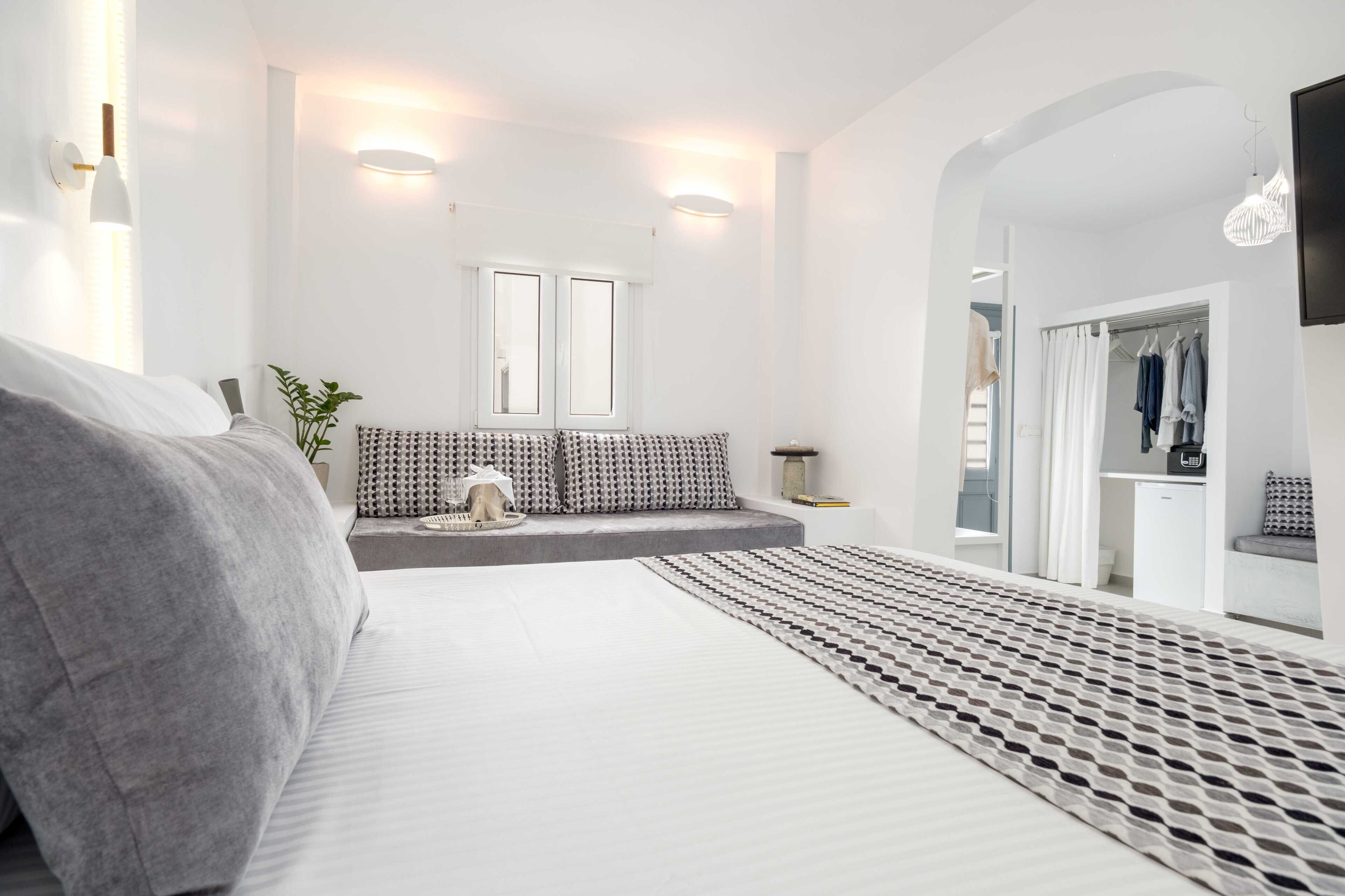 Un dormitorio moderno con una cama, un área de descanso con cojines, una mesita y un televisor montado en la pared.