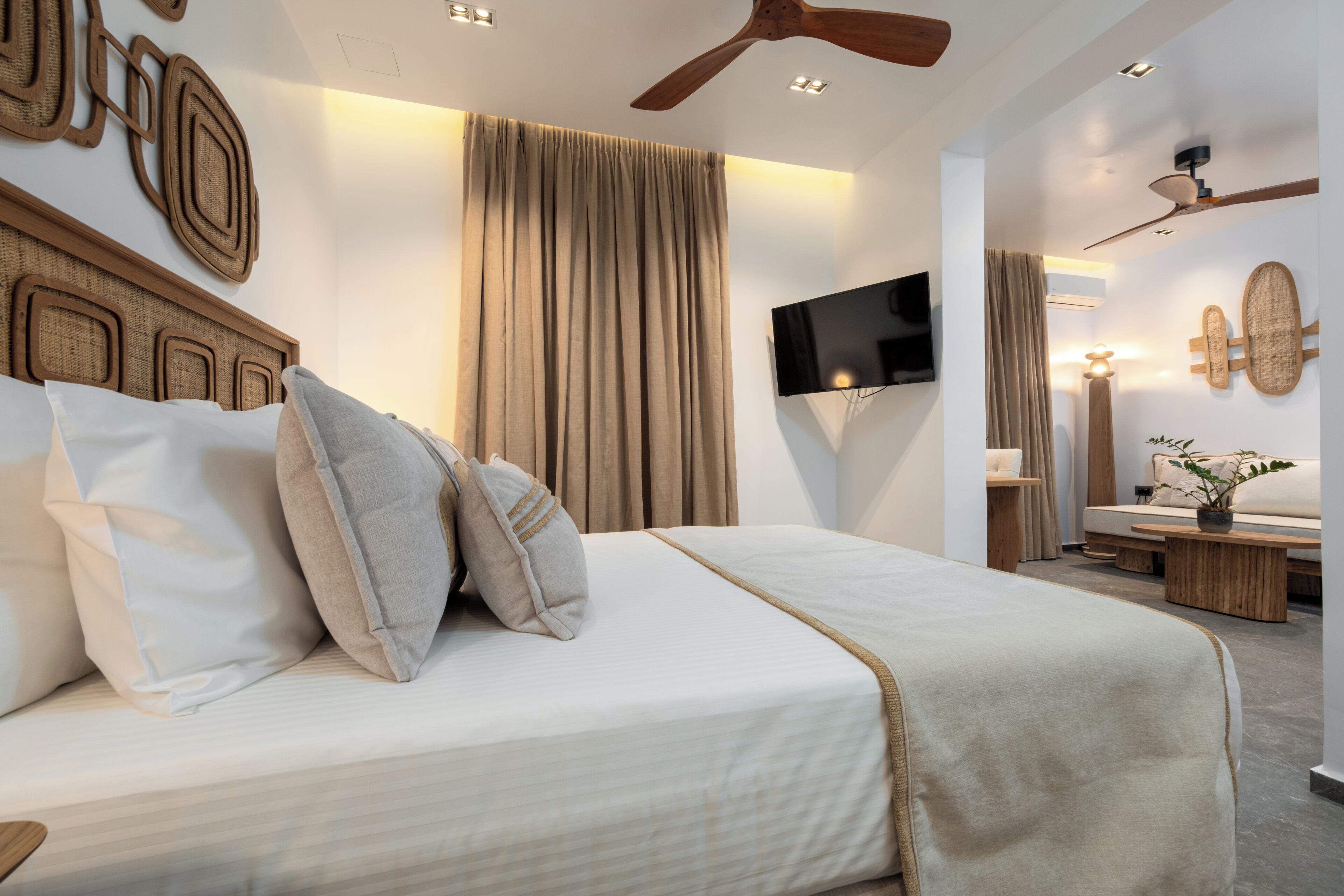 Une chambre moderne avec un grand lit, un ventilateur de plafond, un téléviseur à écran plat et un téléviseur fixé au mur.