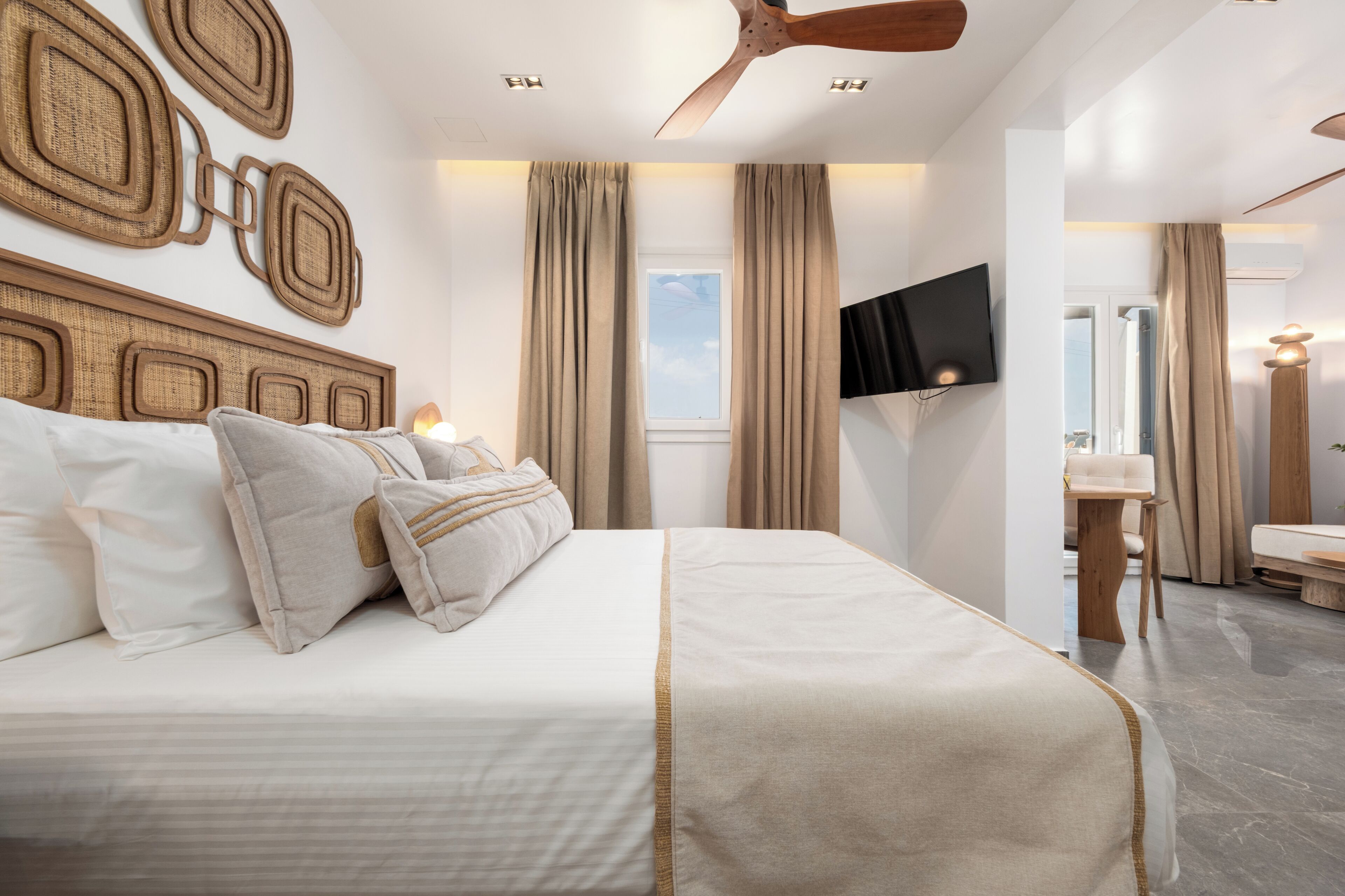A modern hotel room with a large bed, a ceiling fan, a flat-screen TV, and a window with curtains.