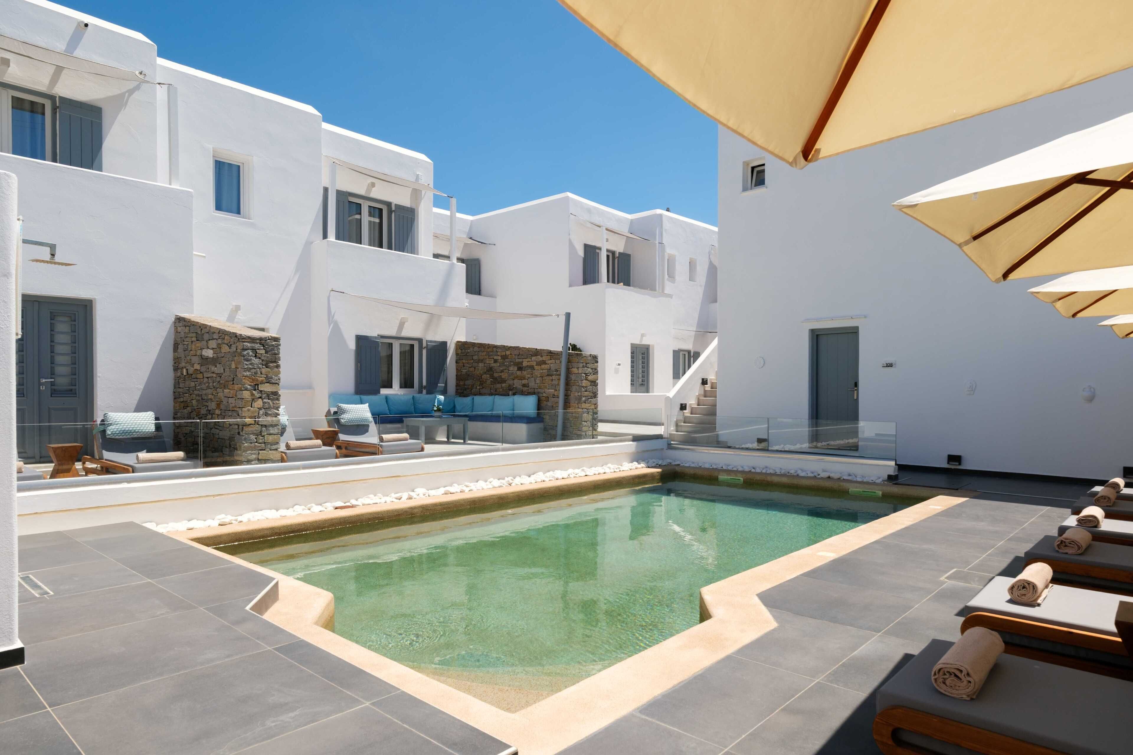 A poolside area with white buildings, stone walls, and lounge chairs.