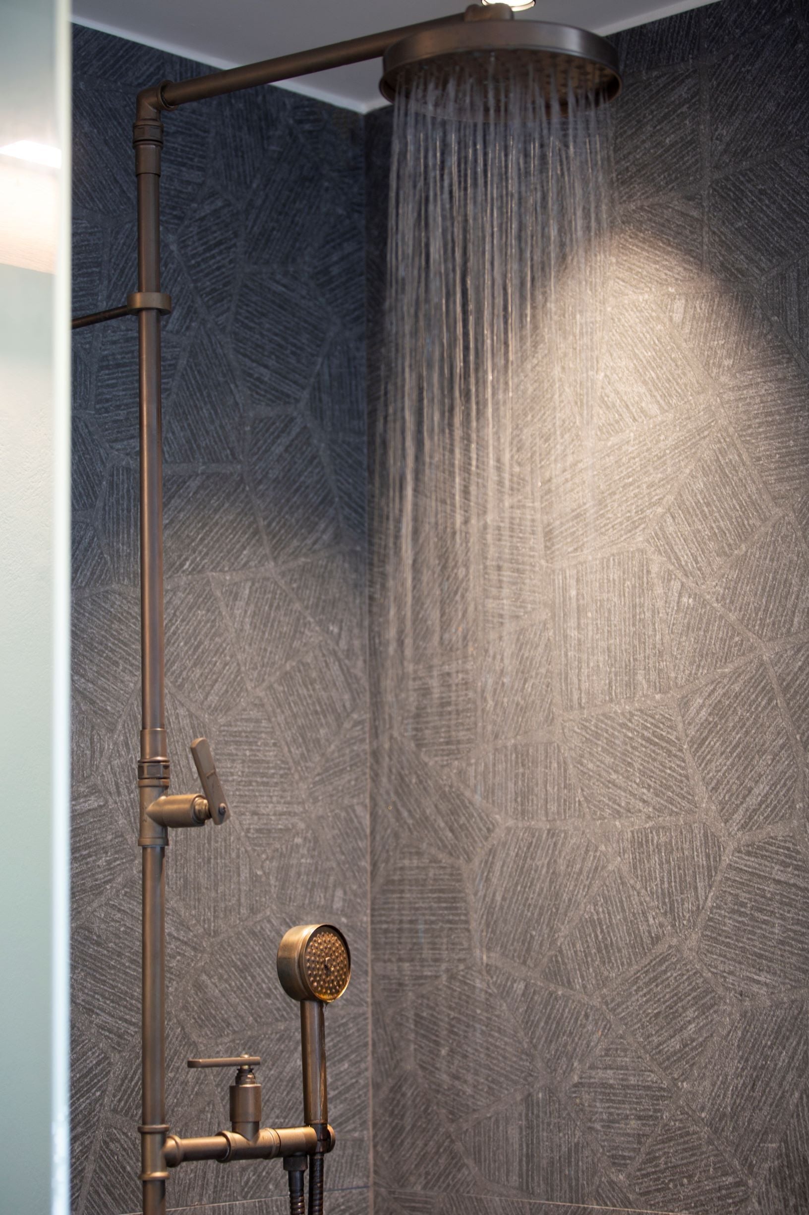 A shower with a vertical rain showerhead and a handheld showerhead, set against a textured wall.