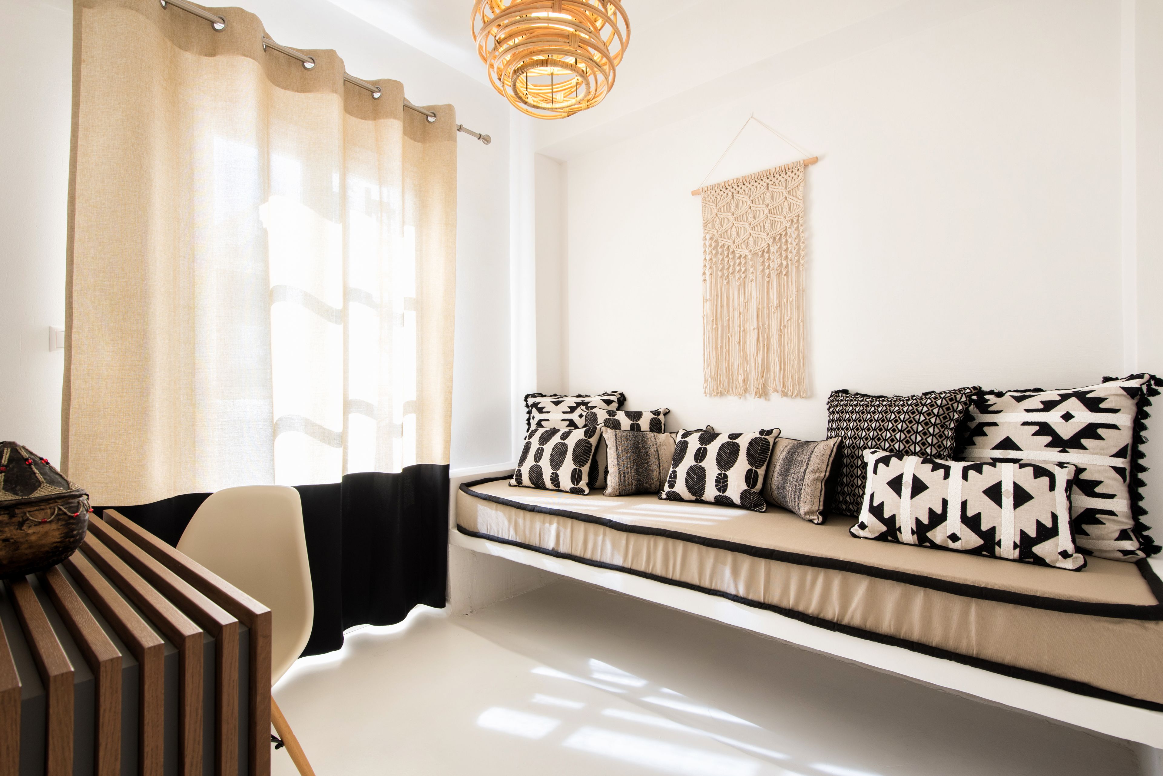 A modern living room with a sofa bed, a hanging macrame wall decor, and a wooden side table.