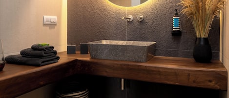 Un baño moderno con un espejo redondo, encimera de madera y dos cestas de mimbre.