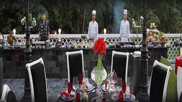 A formal outdoor dining setup with tables set for a meal, surrounded by lush greenery.