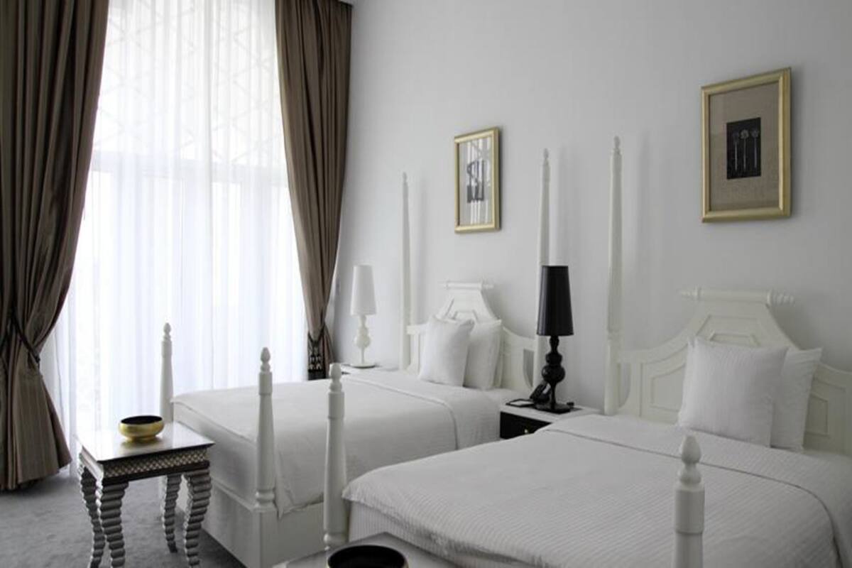 A hotel room with two beds, white bedding, a small table with a bowl, a lamp, and framed pictures on the wall.