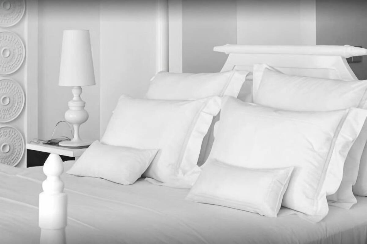 A monochrome hotel room with a neatly made bed, a bedside table with a lamp, and a wall with circular patterns.