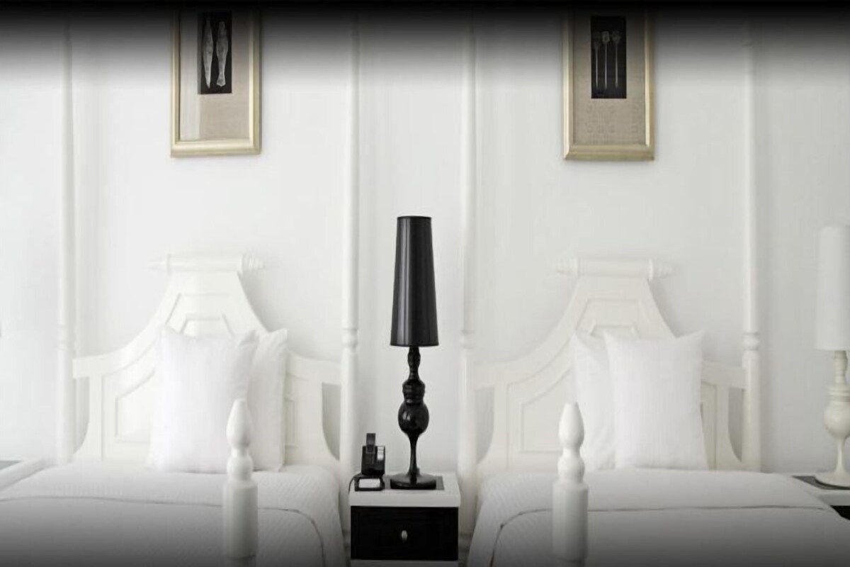 A hotel room with two beds, white bedding, a black lamp on each nightstand, and framed pictures on the wall.