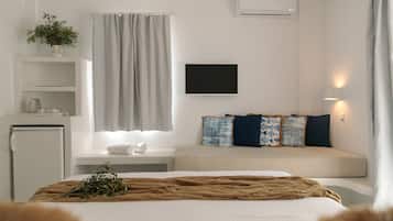 A modern hotel room with a bed, a small kitchenette, a TV, and a window with curtains.