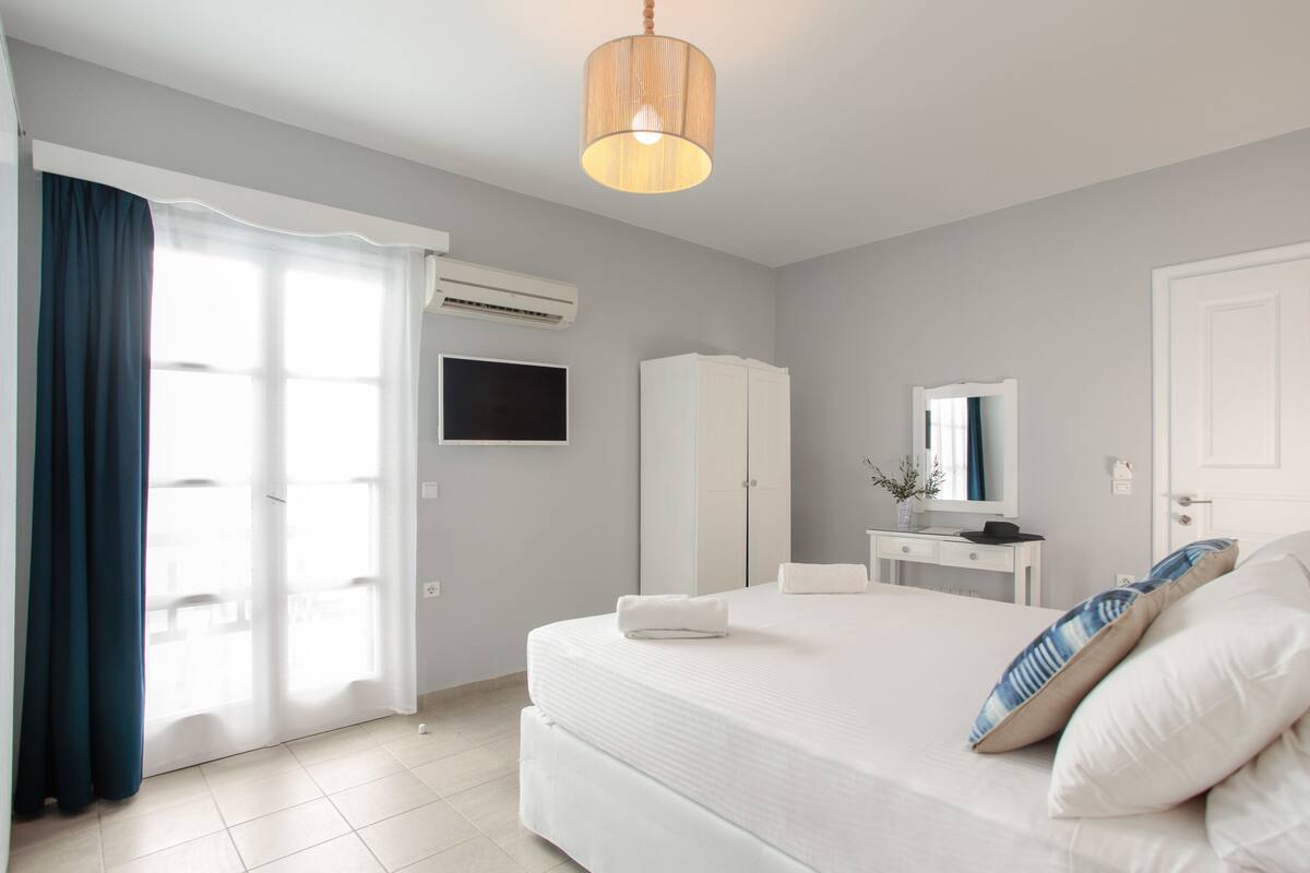 A bedroom with a bed, a desk, a wardrobe, and a television.