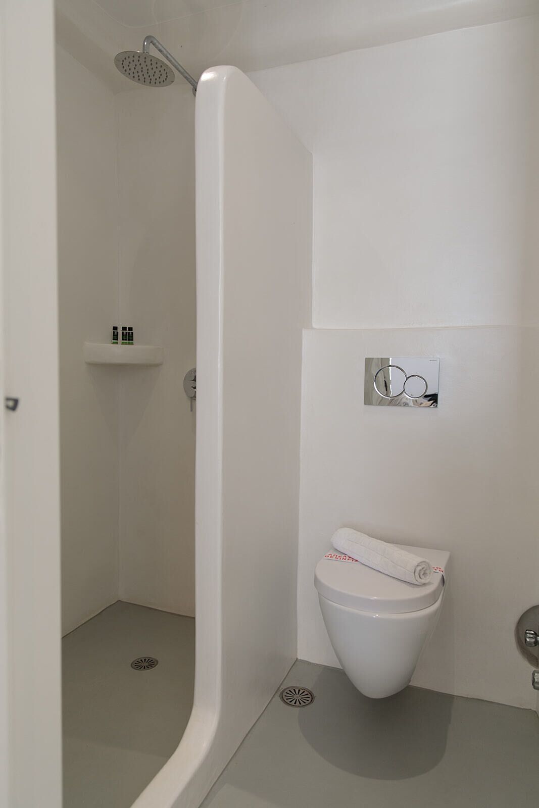 A modern bathroom with a shower, toilet, and a small shelf with toiletries.