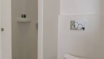 A modern bathroom with a shower, toilet, and a small shelf with toiletries.