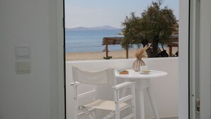 A balcony with a white chair and table, overlooking a beach with a mountain in the distance. - Ippokampos Beachfront (Naxos)