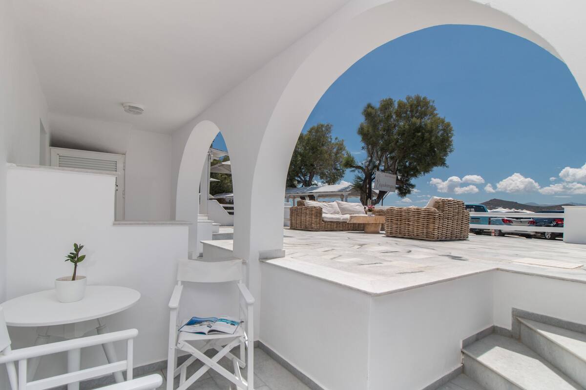 A white interior with a view of the sea, a small table with a plant, and wicker furniture.
