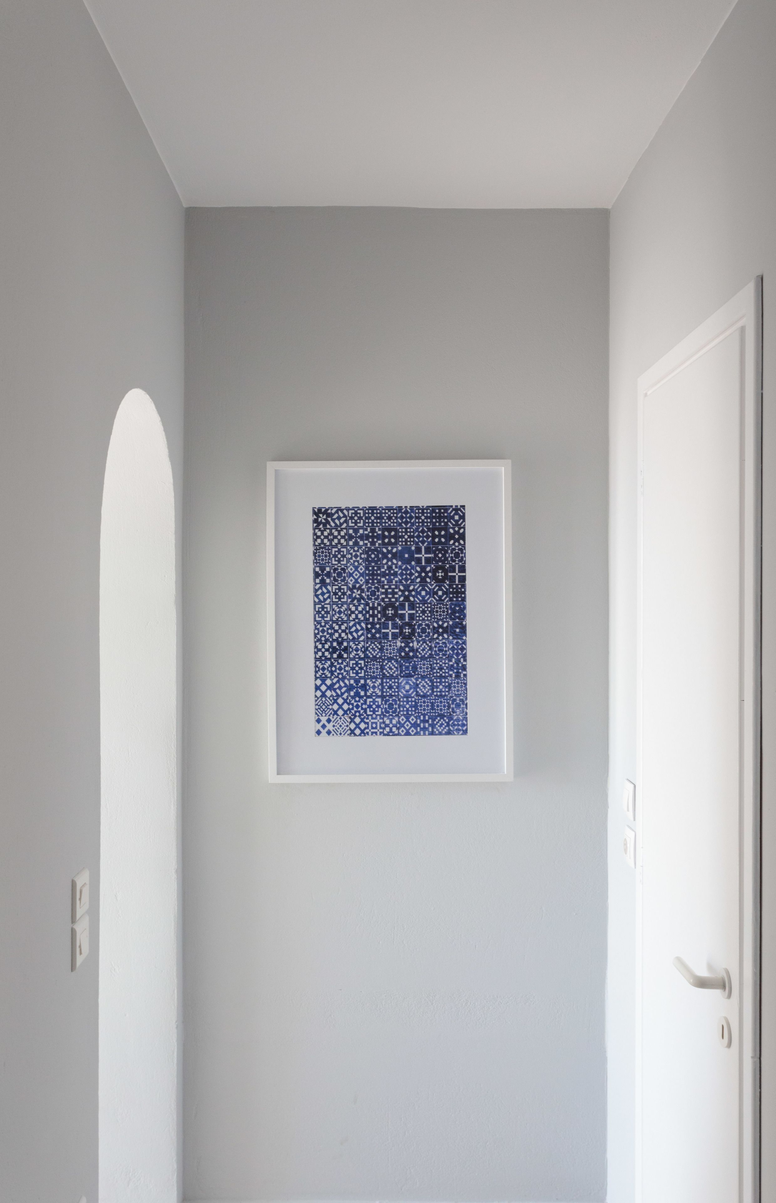 Obra de arte abstracta enmarcada sobre una pared gris claro en una habitación con puerta y arco de color blanco.