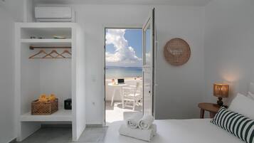 Habitación de hotel con cama, mesita de noche con lámpara, armario, pequeño balcón con mesa y sillas, y vista a la playa.