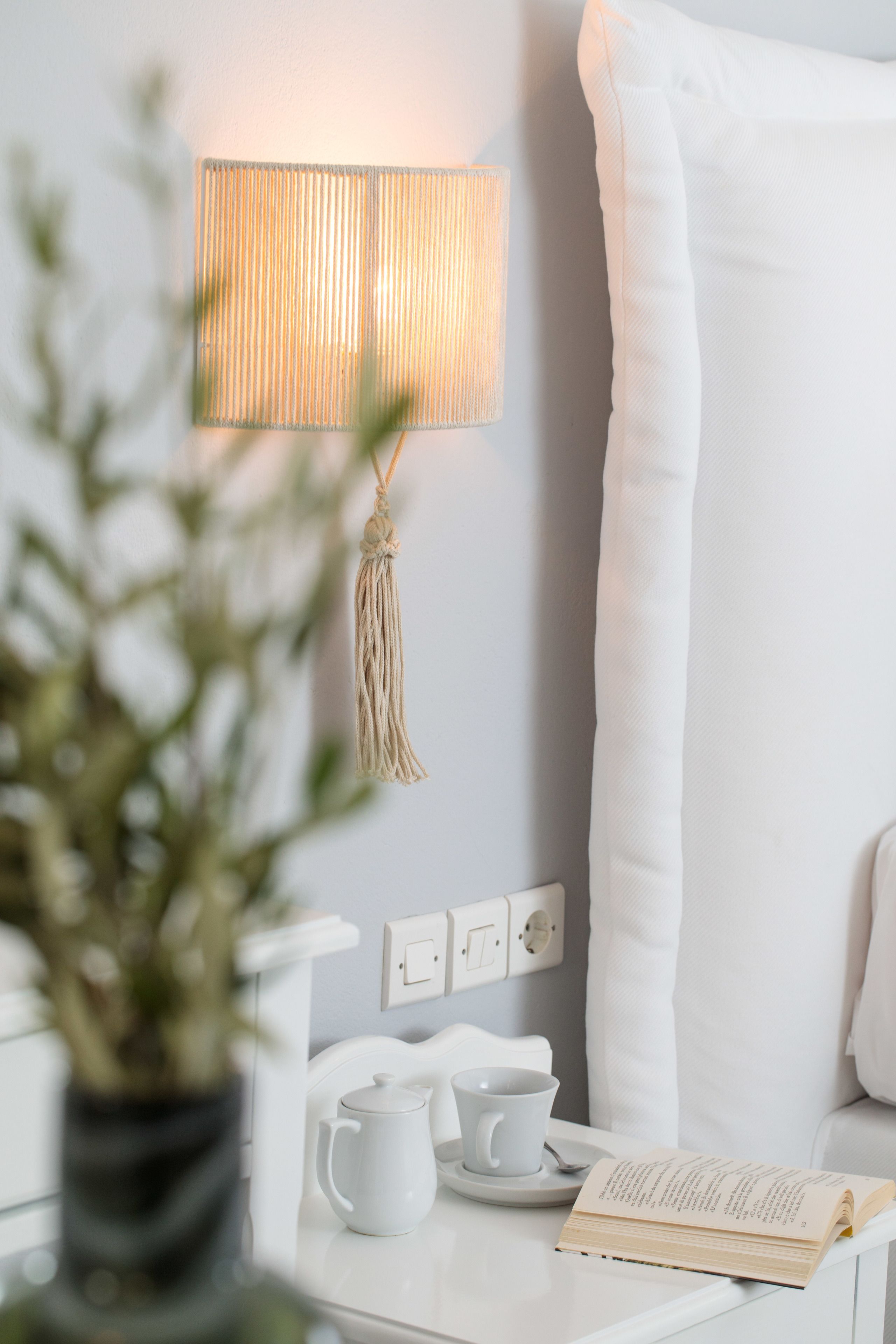 Un dormitorio ordenado con una mesita de noche, una lámpara, un libro y una taza.