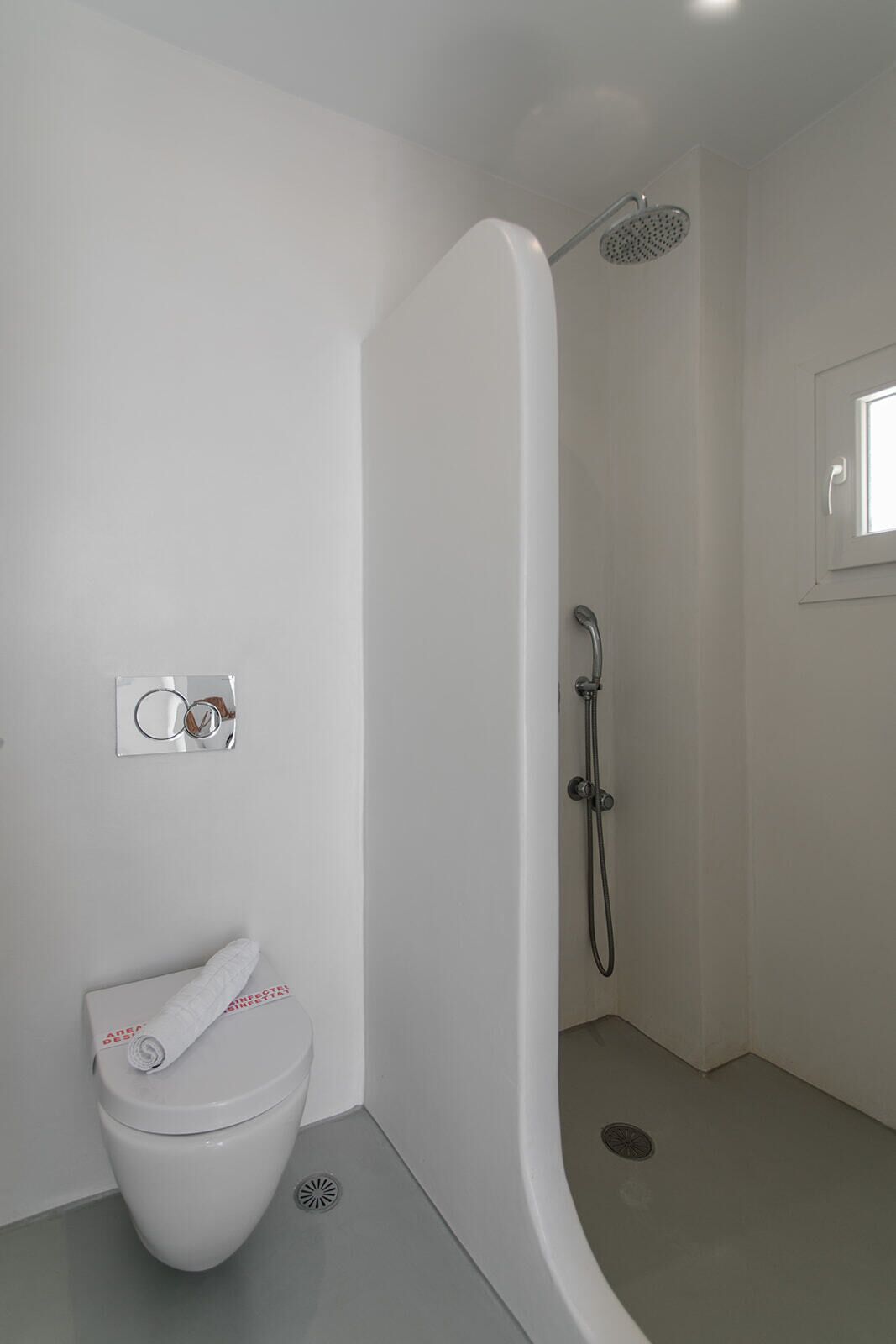 A modern bathroom with a white toilet, a shower with a handheld showerhead, and a small window.