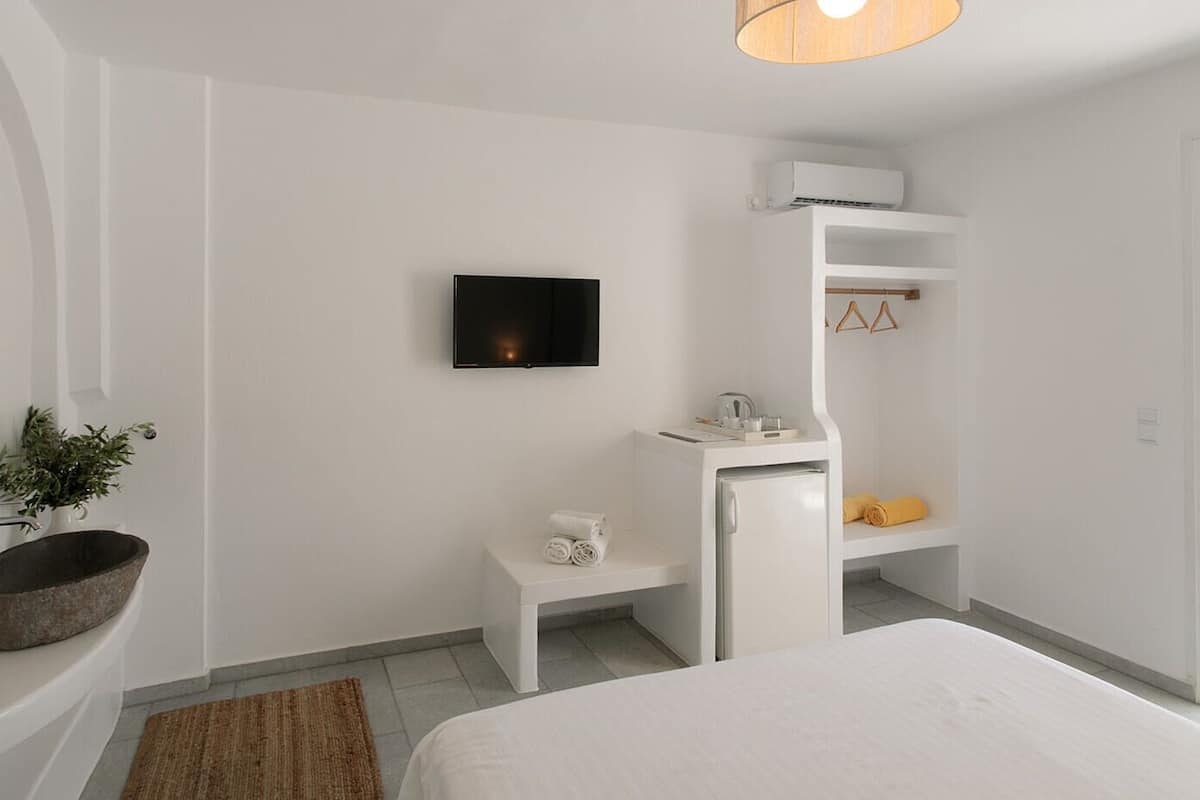 A modern bedroom with a bed, a small white desk, a built-in TV, and a white wardrobe with a mirror.