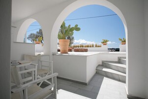 Una terraza exterior blanca con zona de estar, una planta grande en maceta y vistas al cielo.