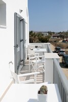 A balcony with white furniture, a potted plant, and a view of parked cars and buildings in the distance.