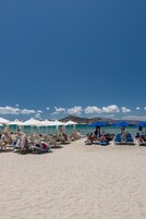 Una playa con filas de tumbonas y sombrillas, cielo despejado y una montaña a lo lejos.