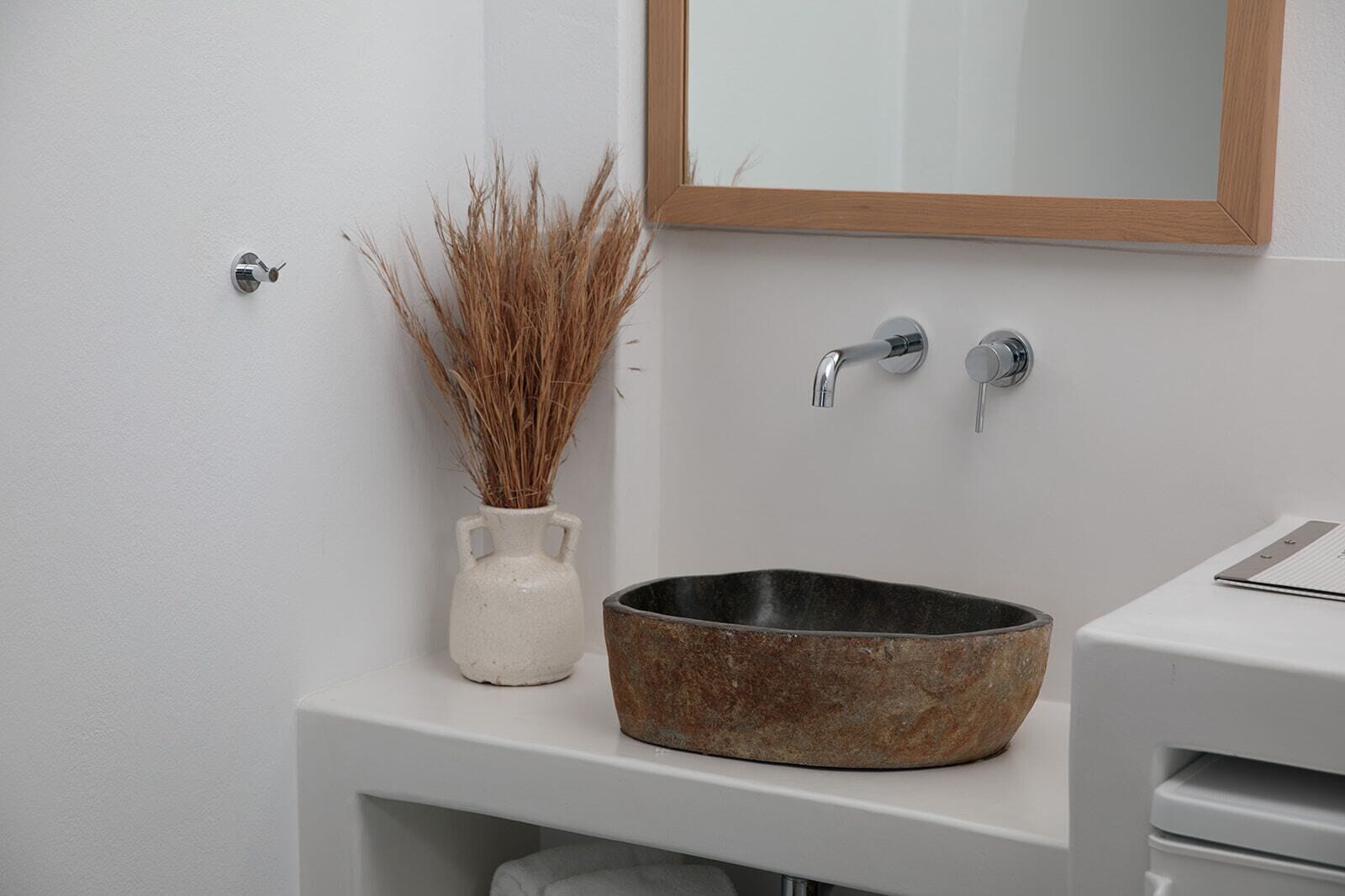A bathroom with a white sink, a wooden-framed mirror, and a vase with dried plants.