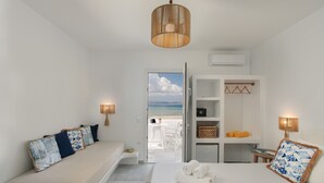 A hotel room with a bed, a seating area with cushions, a wardrobe, and a view of the beach. - Ippokampos Beachfront (Naxos)