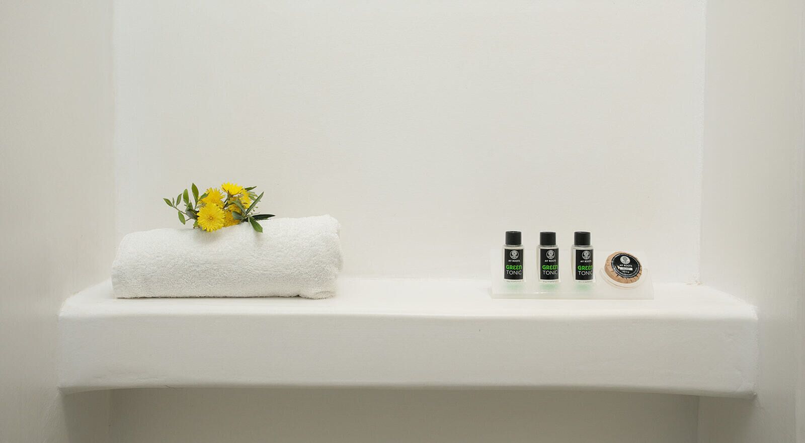 A bathroom shelf with a white towel, a small bouquet of yellow flowers, and three bottles of green body tonic.