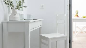 Un baño blanco con espejo, lavamanos, una silla y una mesa con frutas.
