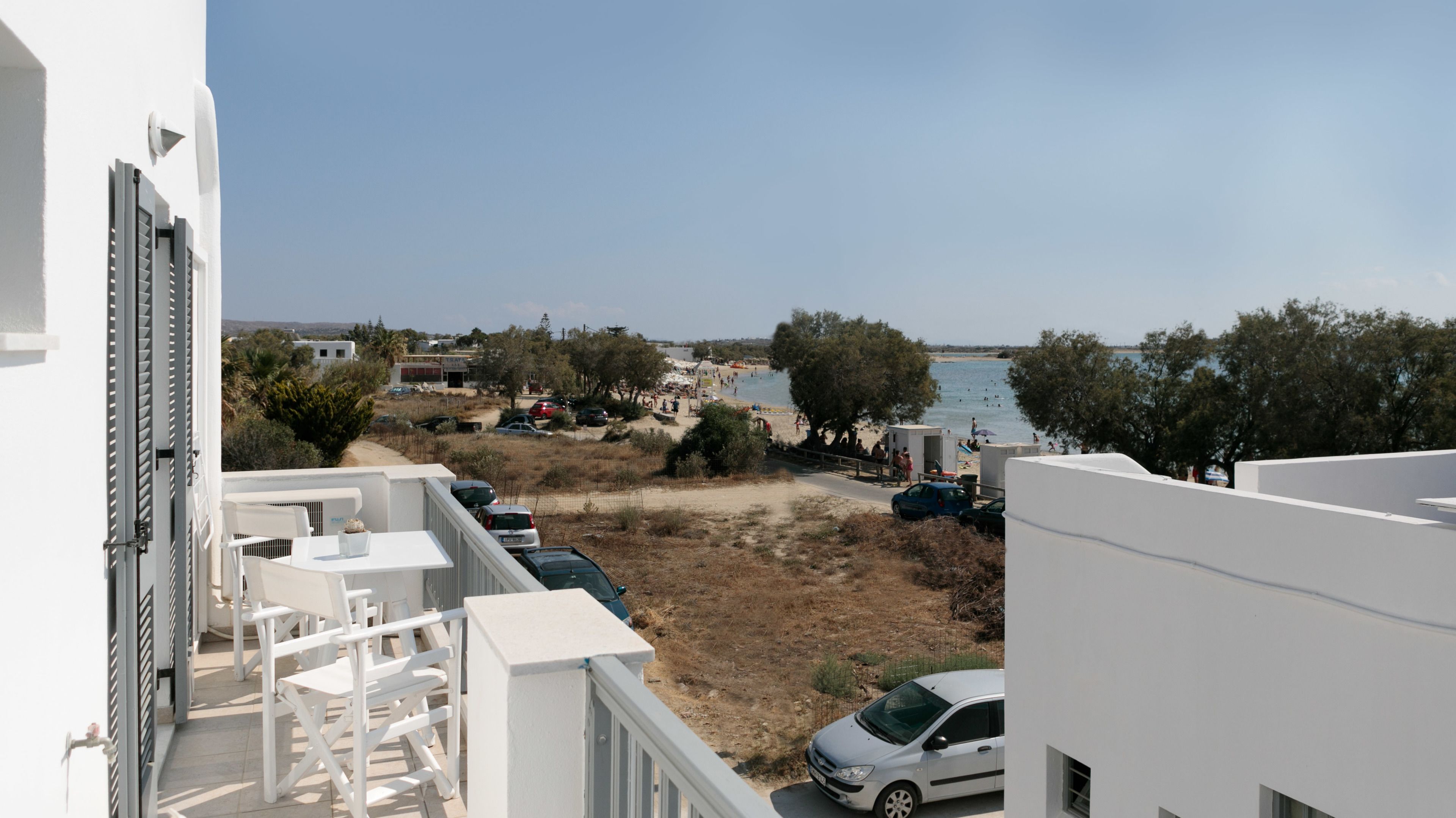 Blick auf die Küste mit Strand, geparkten Autos und einem weißen Gebäude mit Balkon.
