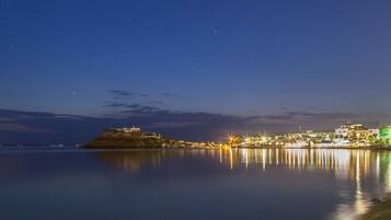 A calm waterfront at night with buildings and a hill in the background.