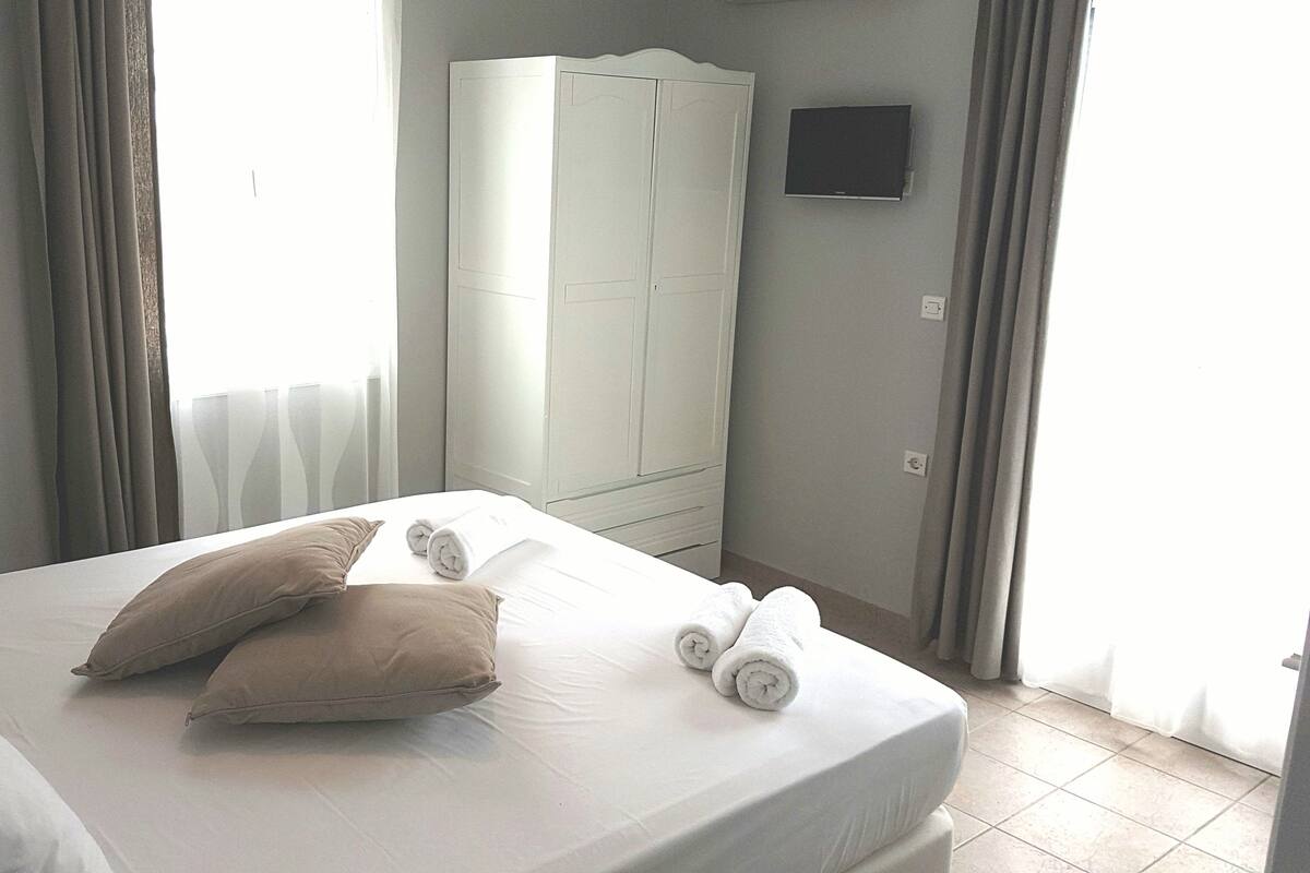 A neatly made bed with pillows and rolled towels, a wardrobe, and a television on the wall.