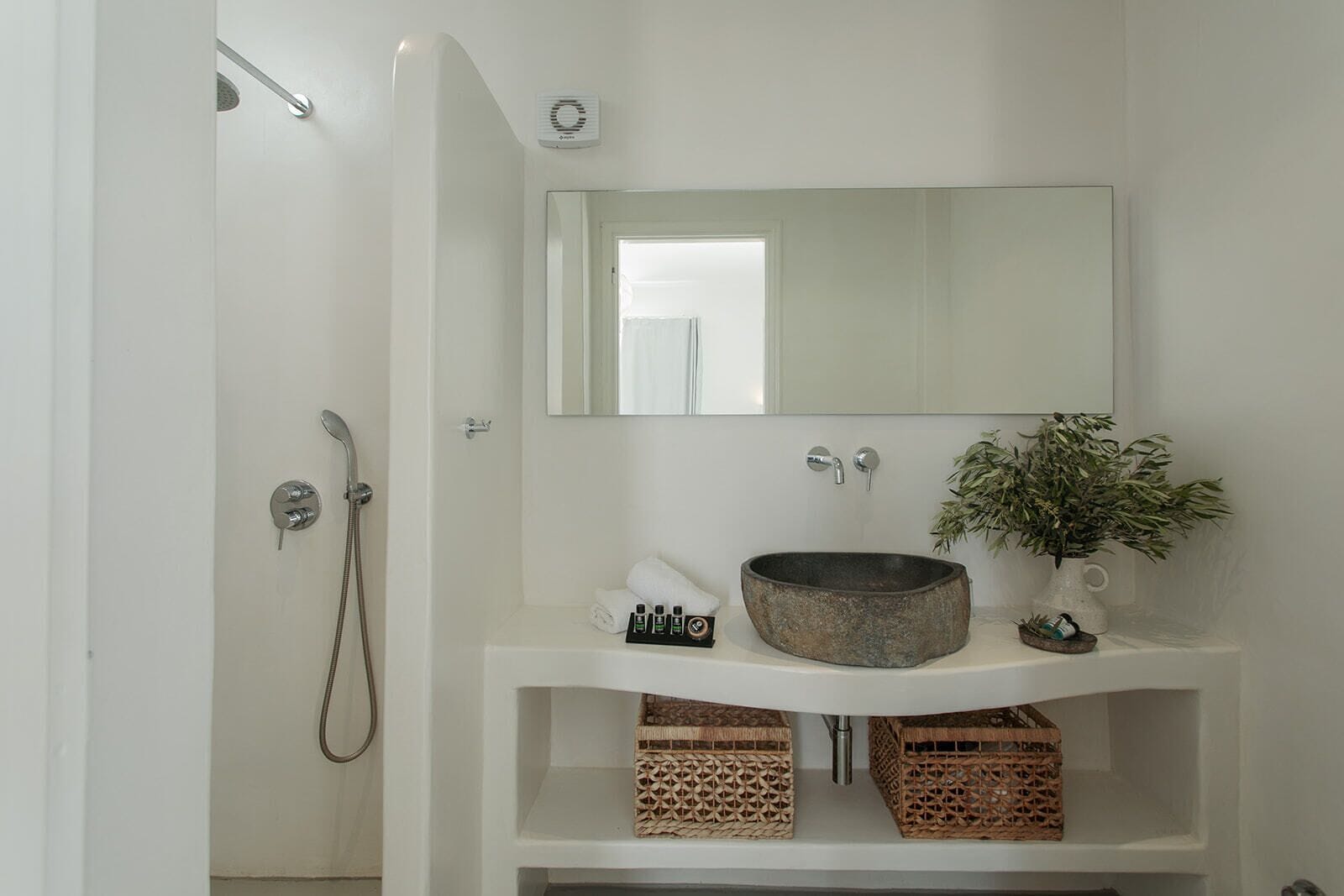 Une salle de bain avec un lavabo blanc, un grand miroir, une douche et une plante en pot.