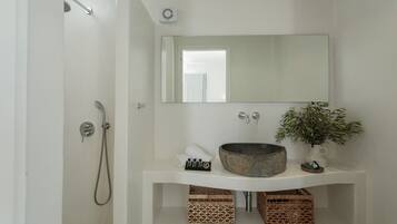 Une salle de bain avec un lavabo blanc, un grand miroir, une douche et une plante en pot.