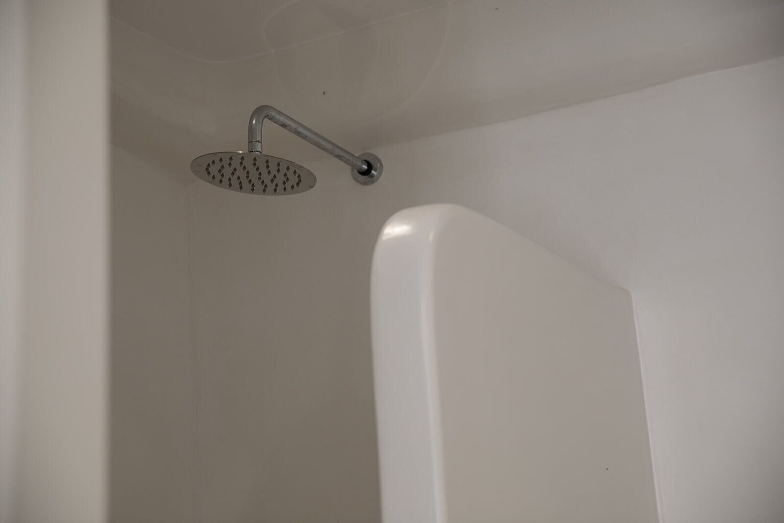 Un área de ducha con cabezal de ducha redondo y una bañera blanca.
