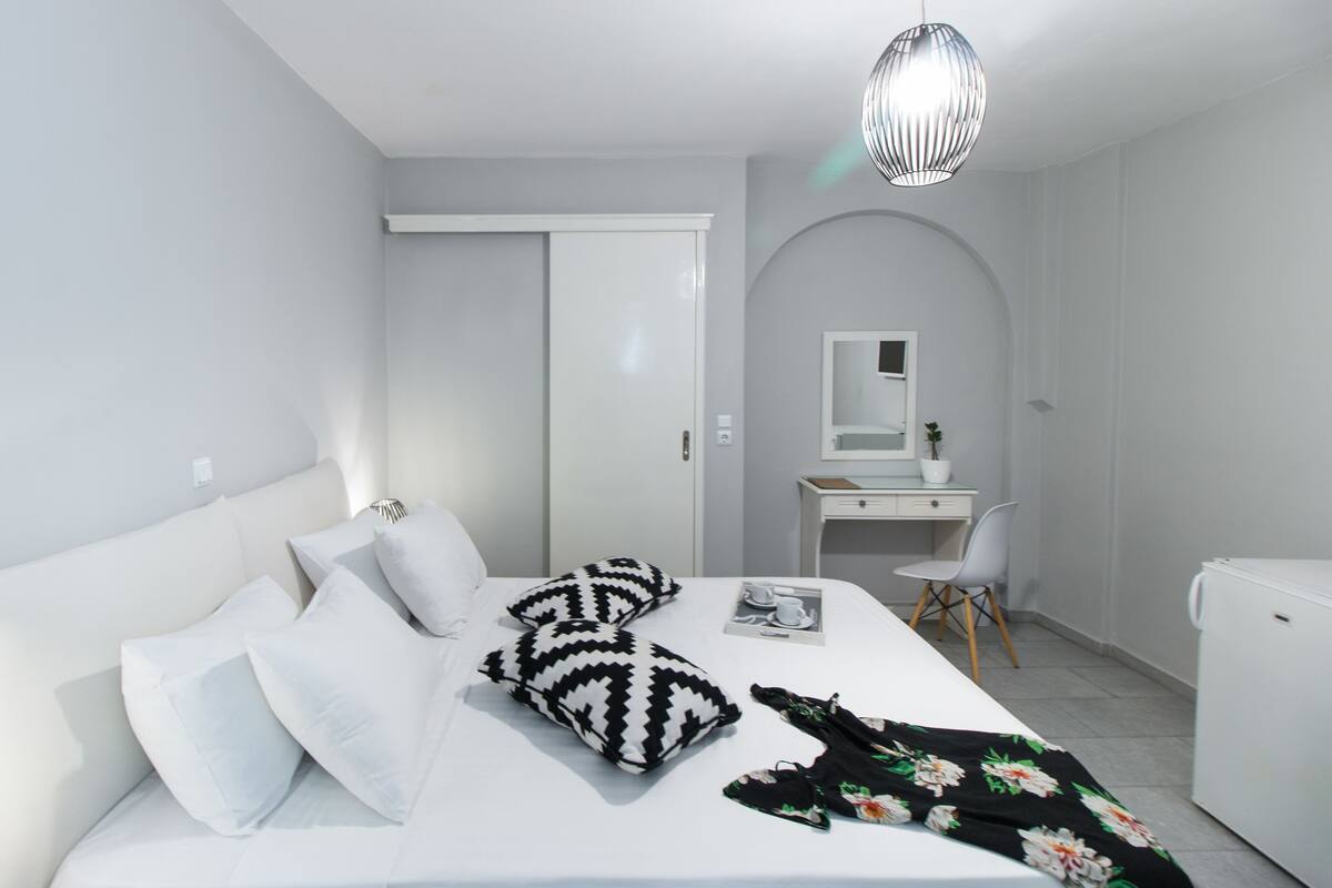 A modern bedroom with a bed, pillows, a desk, a chair, a mirror, and a hanging light fixture.