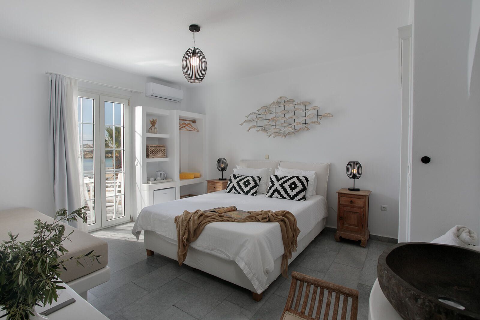 A modern bedroom with a bed, bedside tables, a wooden bench, a large window, and a view of the outdoors.