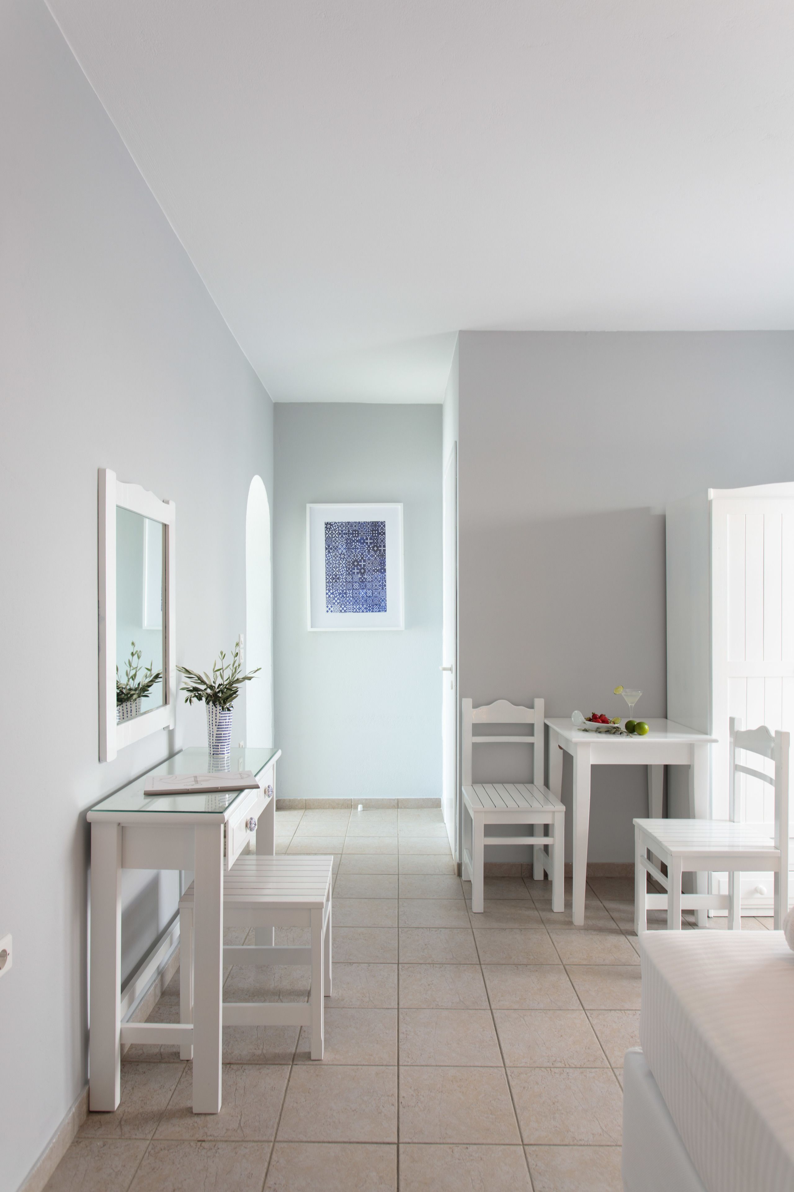 A modern, minimalist room with white furniture, a glass table, and a framed artwork on the wall.