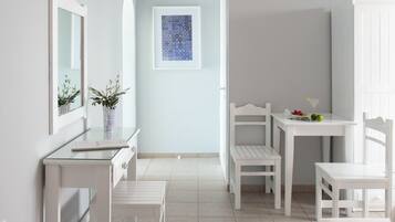 A modern, minimalist room with white furniture, a glass table, and a framed artwork on the wall.