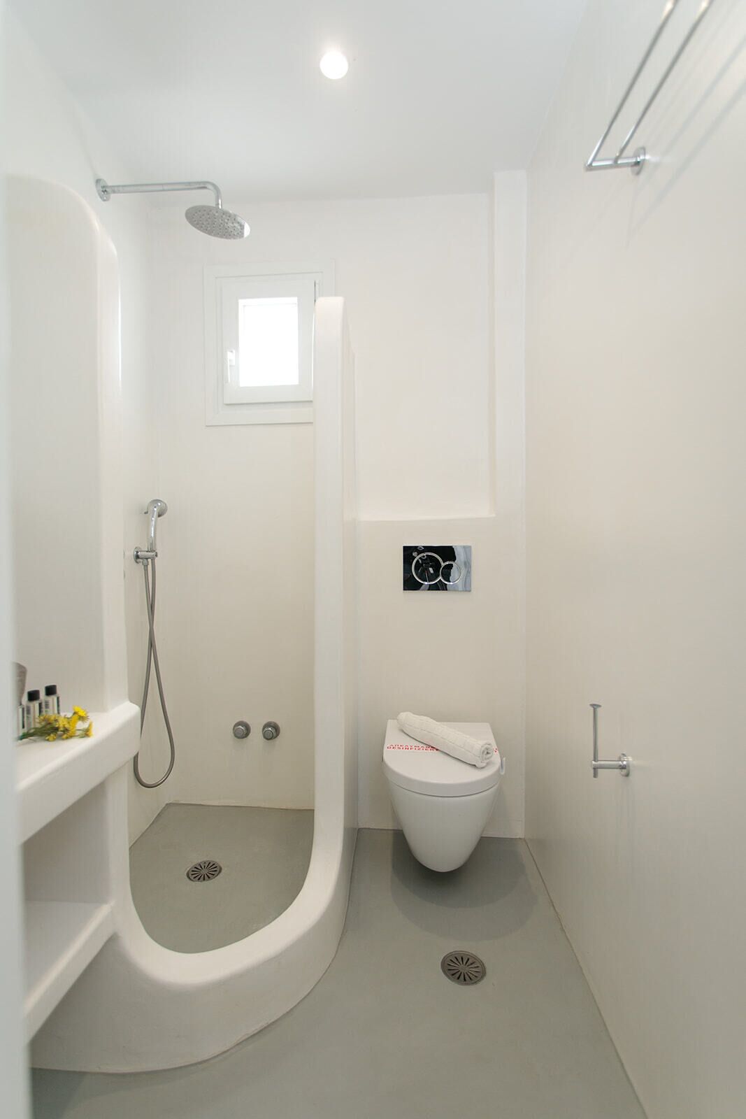 A modern bathroom with a walk-in shower, a toilet, and a small window.
