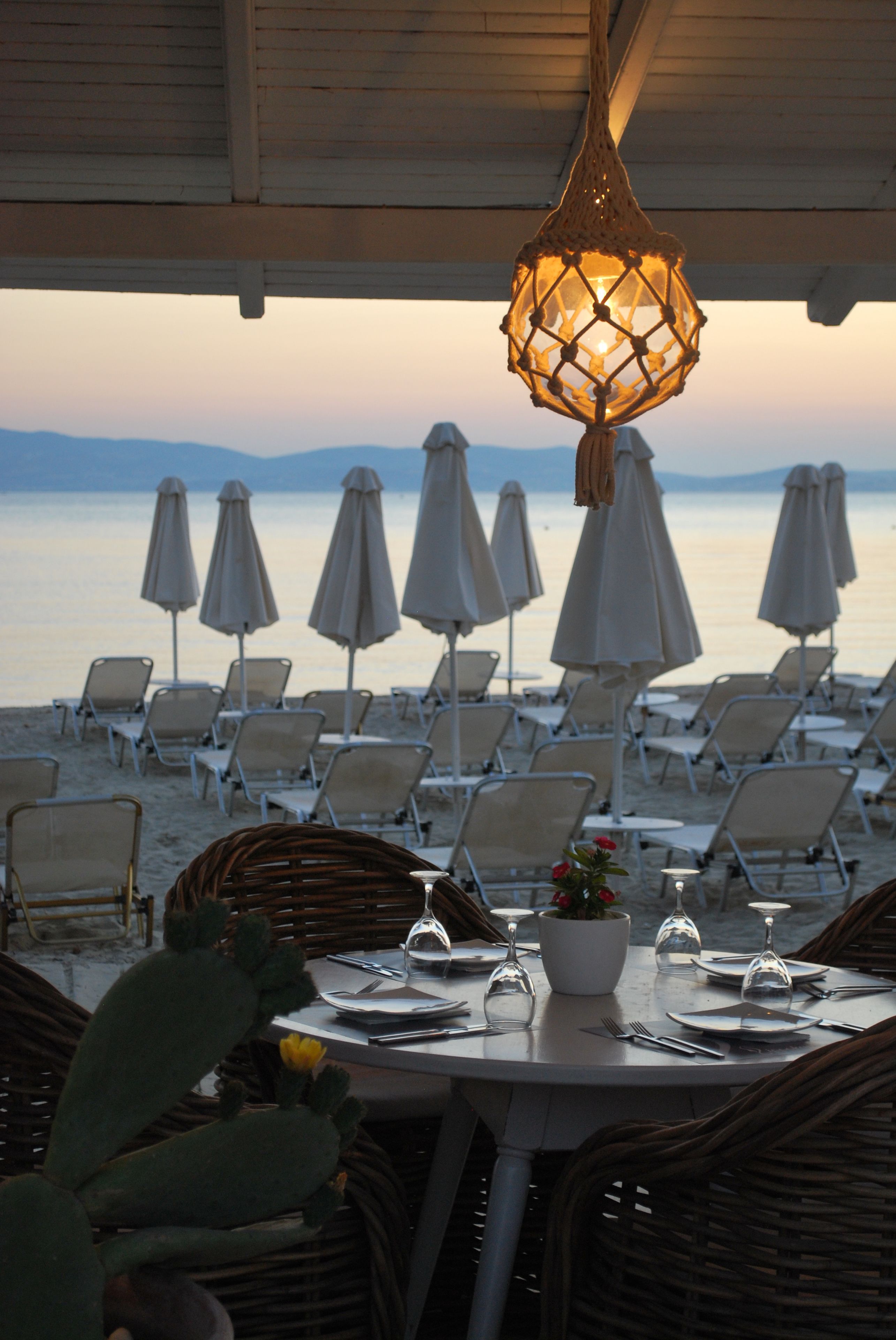 Un espace de restauration situé en bord de mer, avec des chaises et des tables en osier, des parasols et une vue sur la mer.