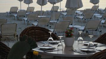 Un espace de restauration situé en bord de mer, avec des chaises et des tables en osier, des parasols et une vue sur la mer.