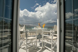 Un balcón con sillas y una mesa blancos, con vistas a un paisaje escénico con nubes y un horizonte lejano.