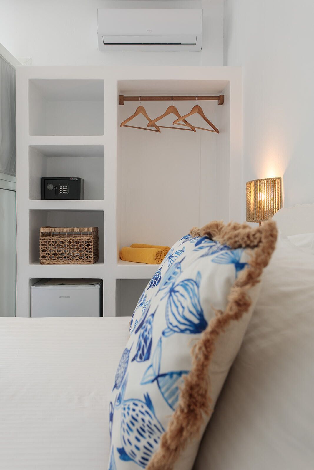 A neatly organized bedroom with a bed, a white wardrobe with shelves, a hanging rack, a bedside lamp, and a small radio.